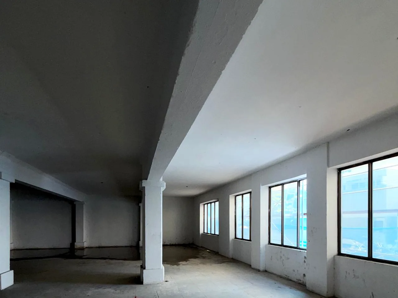 Representative image: empty, unfurnished interior with painted walls, ceiling, and column, and a row of tall dark-framed windows along one wall