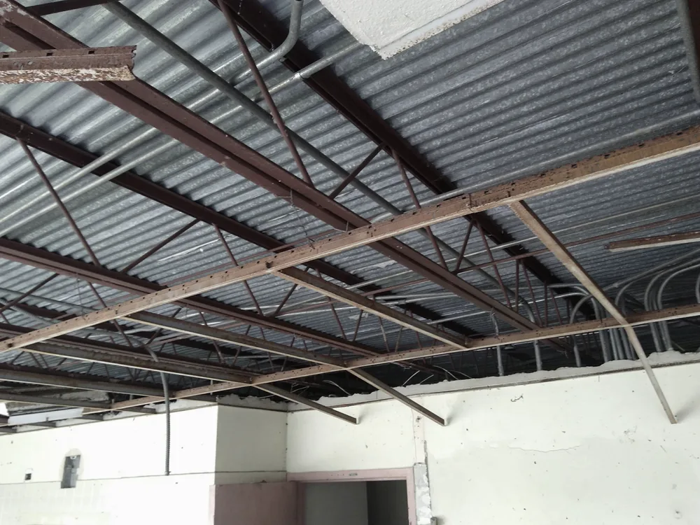 Corroding steel roof framing, joists, purlins, and metal deck seen from below during a structural inspection