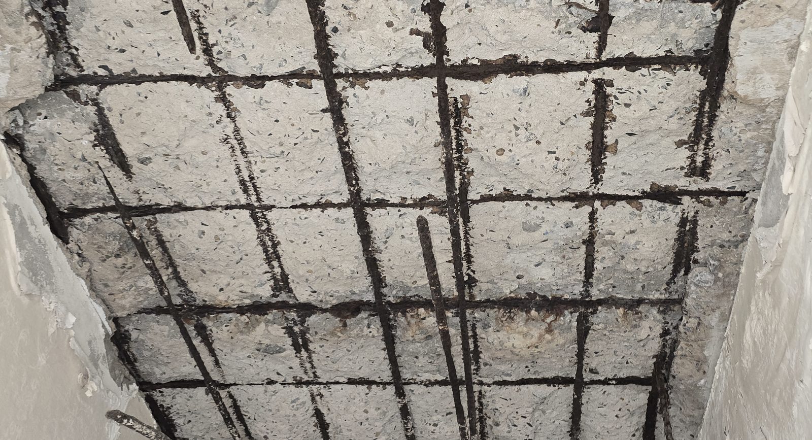 Corroded reinforcing steel exposed in a two-way grid across a concrete soffit where the cover concrete has been lost